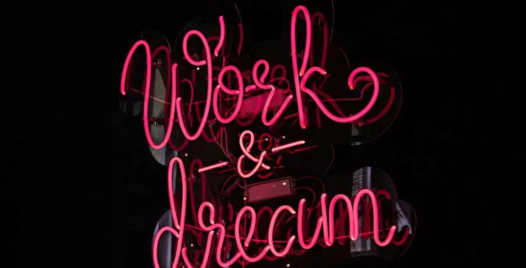 pink neon sign on a black background that says work and dream