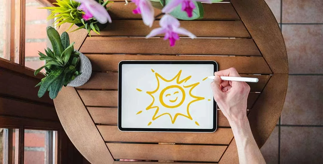 looking down at tablet where someone is drawing a smiling sun image in yellow