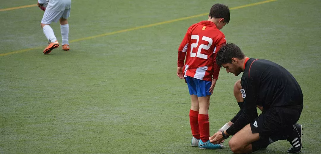 football coach tying shoe lace of young player