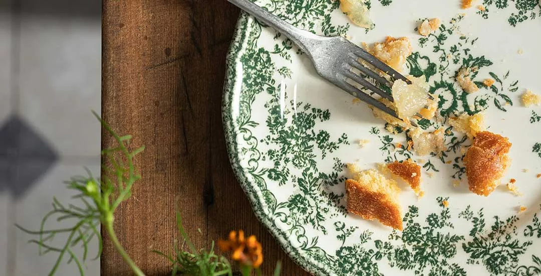 plate with green floral pattern and fork resting on it with crumbs left over from a pice of pie.