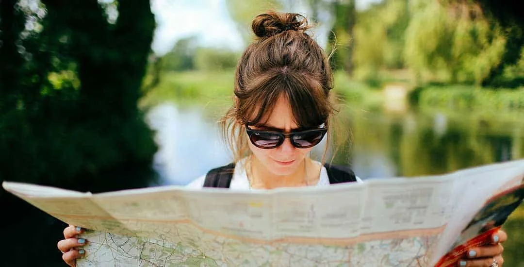 woman wearing sunglasses studying a map outside on a walk