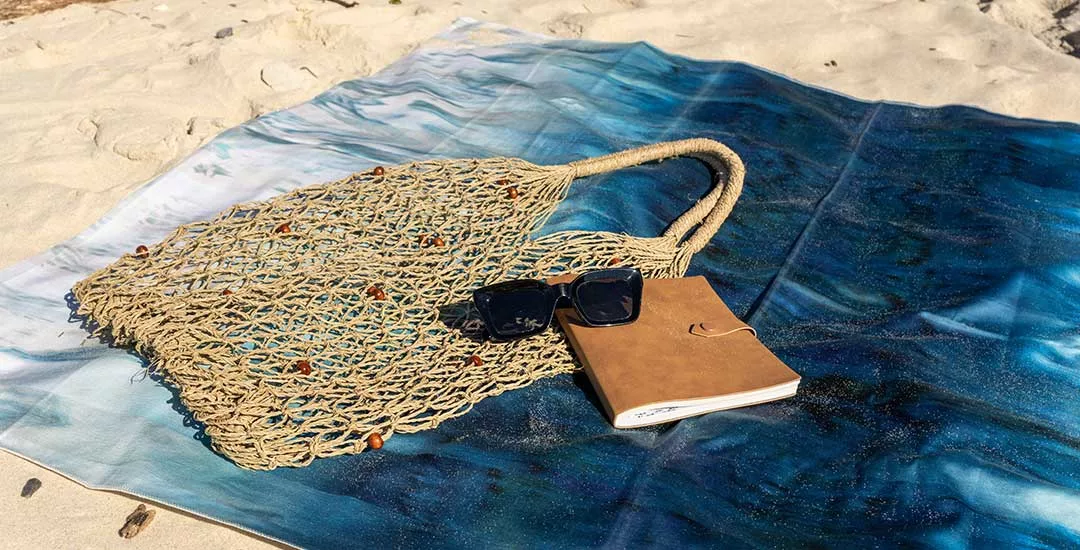 towel, bag, sunglasses and journal sitting on sandy beach