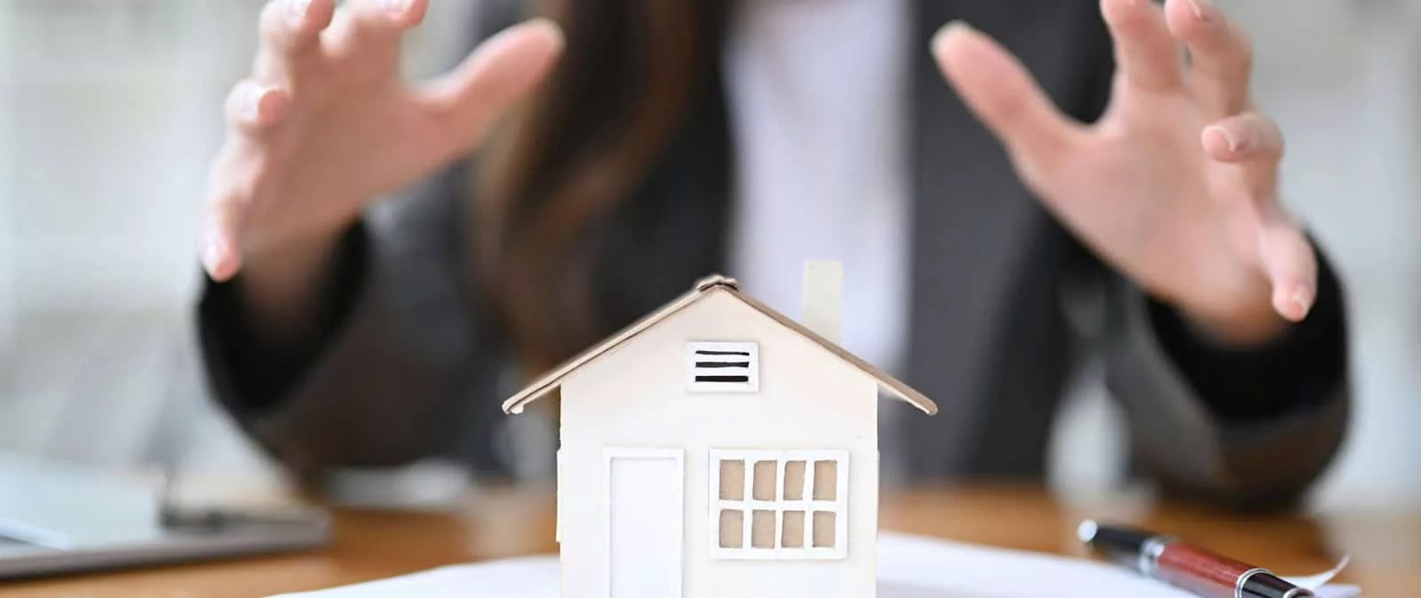 Business professional protecting a miniature house model on a desk, symbolising property ownership and financial security.