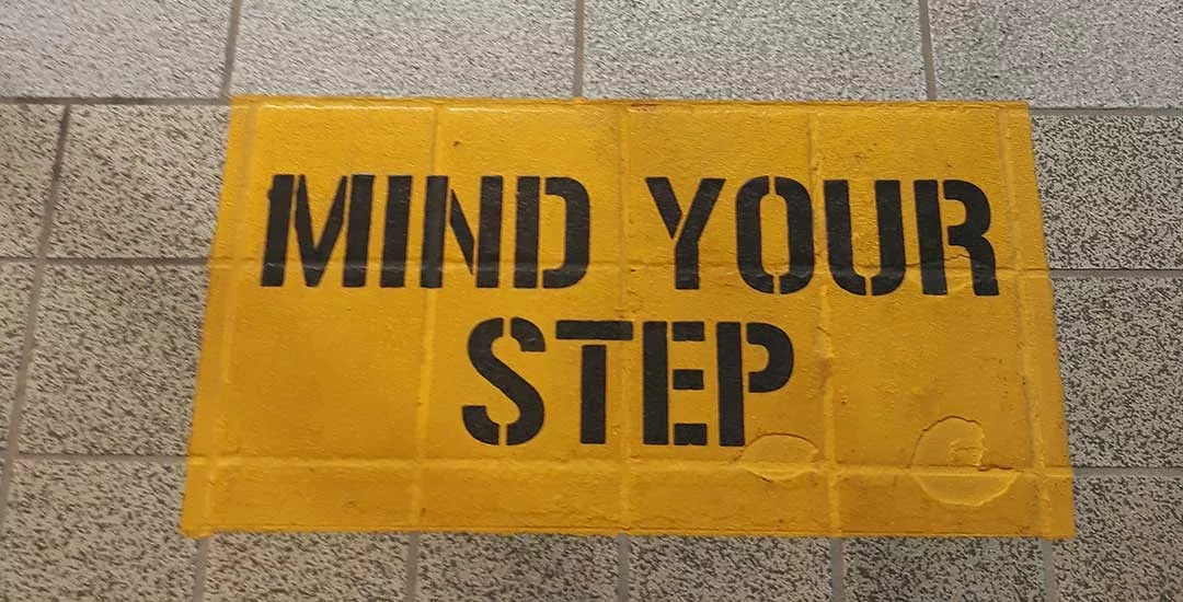 mind your step written on ground in black text on a yellow background