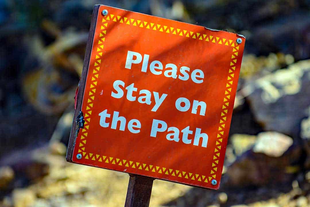 red sign saying 'please stay on the path' in white writing representing the importance of understanding the IR35 rules and how they apply to contractors